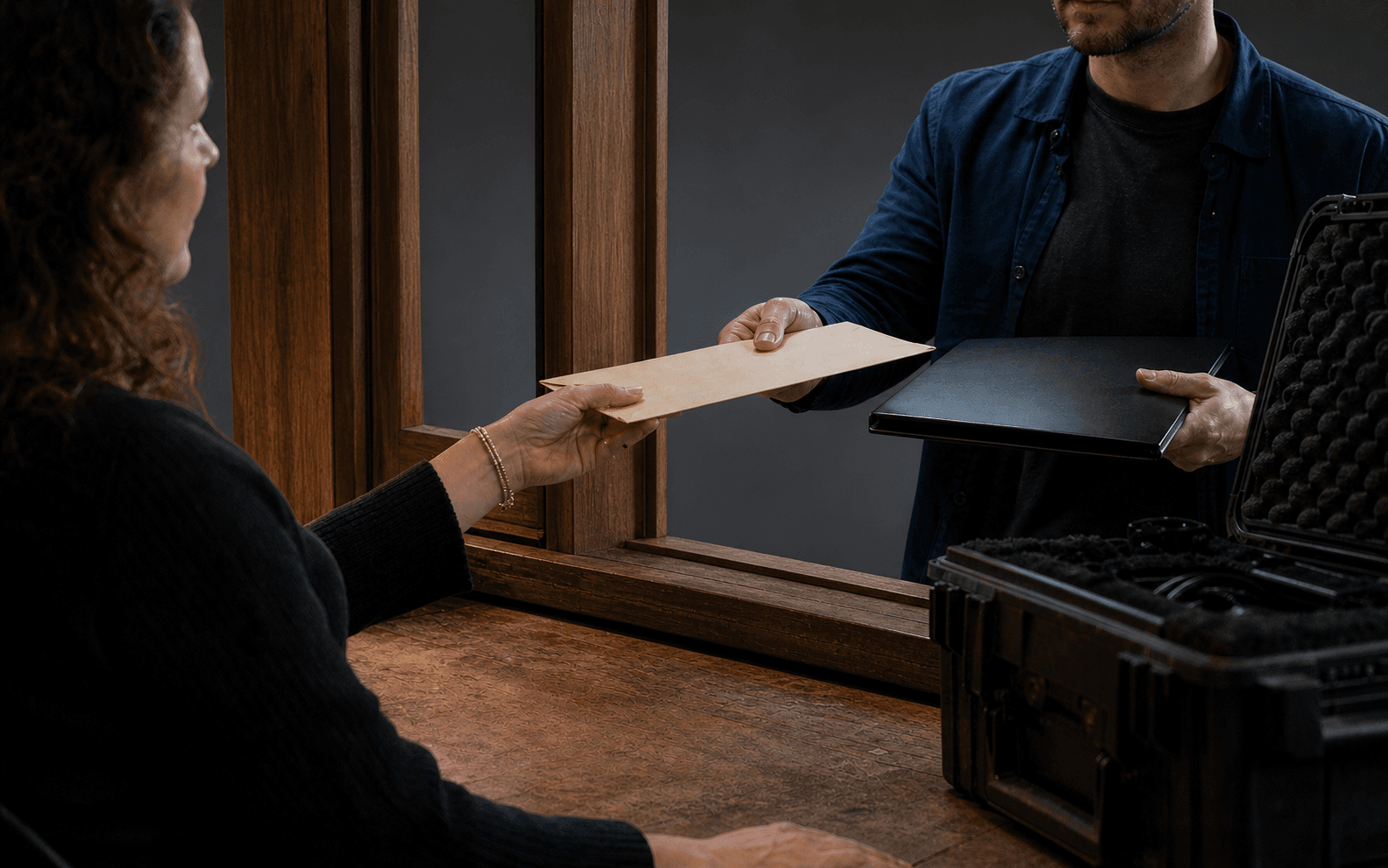Freelancer handing a blank sealed envelope and closed folio across a production service window